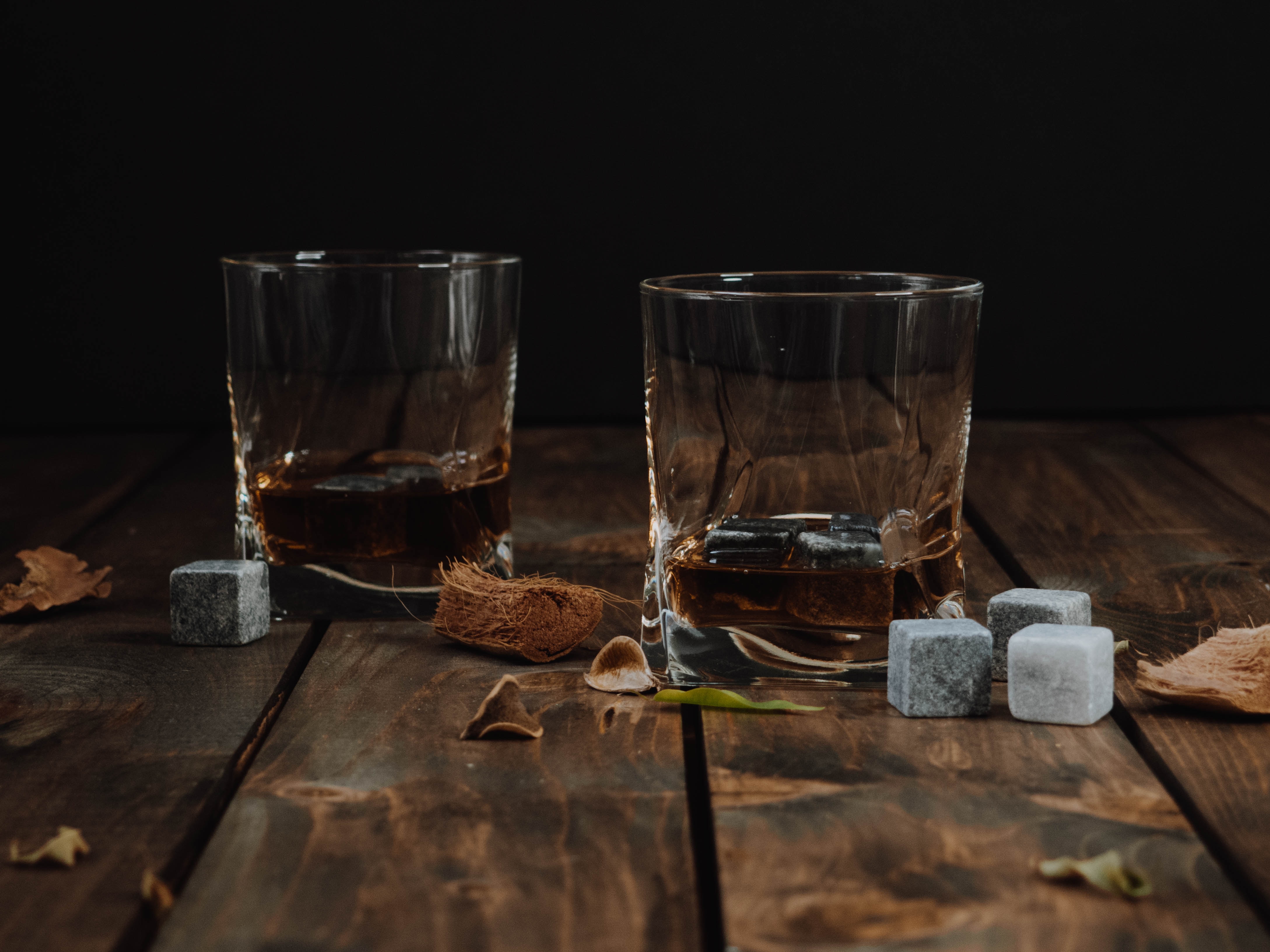 Two whisky glasses on a wooden table with ice cubes